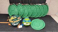 Set of green plastic turtle shells and three Ninja Turtle masks in front.
