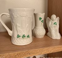 Front view of Belleek mug, vase, and angel figurine showing shamrock details and white porcelain texture.