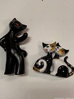 Two cat figurines: one black anthropomorphic cat and one harlequin-style Goebel pair of cats.