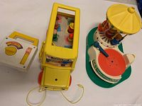 All items in the lot including the yellow school bus with little people, the carousel musical toy, and the square musical radio.