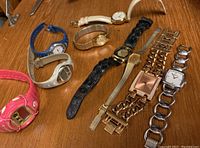 Full lot of 8 assorted ladies watches in various styles and bands on a wooden surface.