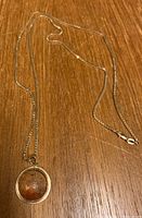 Full view of the 10K gold box chain necklace with pendant on wooden surface