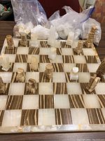 Marble chessboard with pieces arranged on board, some pieces and two bags of extra pieces behind
