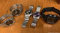 Five men's wristwatches displayed on wooden surface showing variety in style and bands.