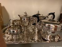 Overall view of silver plate tea and coffee set displayed on an engraved silver tray, showing five vessels including teapot, coffee pot, sugar bowl, creamer, and covered serving bowl.