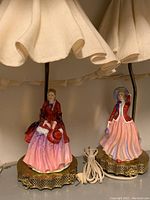 Two vintage Paragon china table lamps, each with fabric shades, visible cords, and detailed porcelain figurine bases depicting women in period costume.