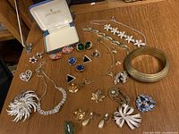 Wide angle photo showing entire vintage jewellery lot with earrings, brooches, necklaces, bracelets, and vintage Trifari box on wooden surface.