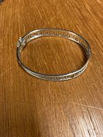 Full view of the hinged bangle bracelet lying flat on wood surface