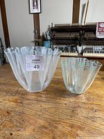 Front view of two clear Lucite handkerchief style vases on wooden surface, one larger and one smaller.