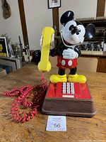 Front view of 1976 Mickey Mouse phone with yellow handset and red cord, on wooden surface.