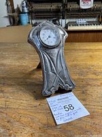 Front view of the antique Art Nouveau sterling silver clock showing the clock face, tarnish, and detailed design along with a note card describing the item.