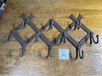 Photo showing antique iron folding coat/hat rack extended flat on a wooden surface with all seven sets of hooks visible.