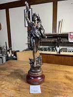 Full view of antique bronze statue on wooden base showing detailed figure of woman holding grapes and staff.