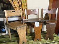 Three antique quarter sawn oak 3-legged chairs and a matching oak shelf arranged with patterned curtains background.