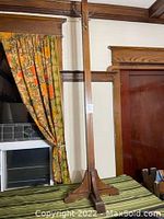 Full vertical view of the quarter sawn oak coat rack with its base and vertical post against a wall with floral curtains.