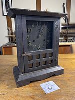 Front view of antique Mission style clock showing stained oak wooden case with door closed and clock face with metal numerals and hands.