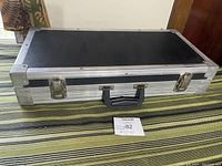 Closed view of the rectangular black hard case with aluminum trim, black handle, and two latch locks on front.