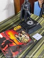 Darth Vader piggy bank with Star Wars book and paperwork on green striped fabric surface