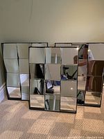 Three multifaceted mirrors with black frames arranged on carpeted floor