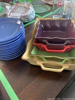 Stack of 12 blue plates and 4 colorful rectangular casserole dishes, largest yellow at bottom