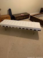 White leather cushioned bench with metal legs, positioned in room showing wear on wood frame