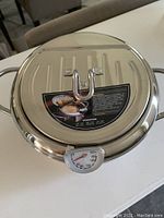 Top-down view of stainless steel lid with integrated thermometer and product information sticker.