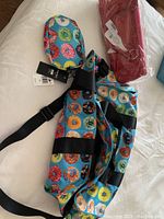 Doughnut print duffel bag with matching small pouch, adjustable black strap seen from an angle on white surface; red packaged wine carrier placed near it.