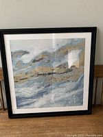 Framed square abstract print in shades of blue, grey and gold with black frame, photo showing the full artwork.
