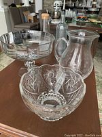 Set of five clear glassware pieces on a table in living area, including bowls, pitcher, and bottles