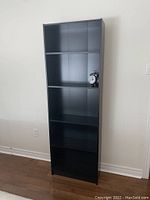 Front view of the black Ikea bookcase showing five shelves and an alarm clock on the second shelf.