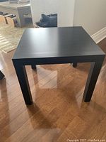 Front and side view of the small black square side table on wood floor, showing simple design and condition.
