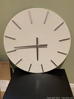 Front view of the round white wall clock with silver markers and hands.
