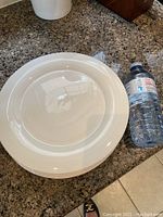 Stack of white dinner plates next to a water bottle for scale, showing the top surface and rim.