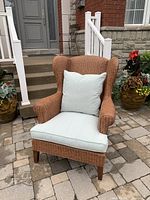 Front view of wicker chair with seat and back cushions on stone patio