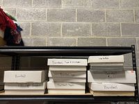 Photo showing 8 cardboard boxes stacked on metal shelving against a concrete wall. Boxes labeled with marker primarily for baseball cards and some football cards.