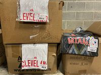 3 boxes of T-shirts including stacks of white Cleveland Indians shirts and packaged dark Miami Marlins shirts with tags visible.