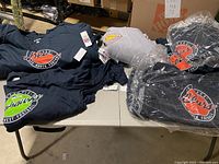 Multiple folded long sleeve NFL shirts laid out on a table including black, gray, navy blue colors with various team logos.