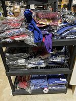 Three-tier metal shelving stocked with stacks of plastic-wrapped shirts, hoodies and jackets in assorted colors