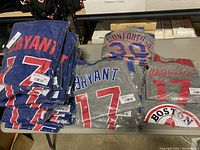 Box with stacks of new MLB baseball shirts featuring player names Bryant, Conforto, and Boston team branding.