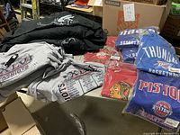 Additional view of gray Patriots XLVI Super Bowl T-shirts stacked with black graphic hoodies on top.