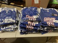 Photo showing packaged blue Colts and Giants women's V neck NFL T-shirts stacked on a table