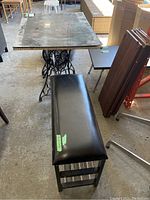 Photo showing the vinyl-covered bench with wood legs and metal shelves beside the table with a Singer sewing machine base and damaged top.
