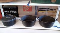 Photo showing three black cast iron pots side by side on a shelf, one with lid and two without lids.