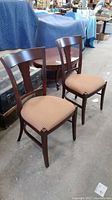 Two dark wood side chairs with upholstered seats in light brown patterned fabric photographed from side angle showing design and condition.