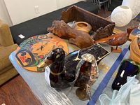 Photo showing all items on table including Indigenous art clock, carved wooden lion, carved wooden duck, wooden bowl, carved wooden shelf, decorative glass duck and cloaked figure.