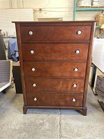Front view of wood and pressboard dresser showing five drawers and silver-tone round knobs.