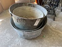 Four nested metal tubs showing varying sizes and wear, stacked inside each other on a concrete floor.