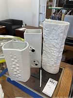 Three white ceramic vases with varying textures on a glass-topped table.