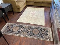 Full view of two rugs side by side on wood floor: cream 4x6 throw and black 2x6 runner