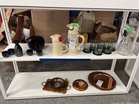 Full view of all items on two shelves showing saki set, beer steins, glasses, decanter, wooden bowl with spoon, and additional dishes.